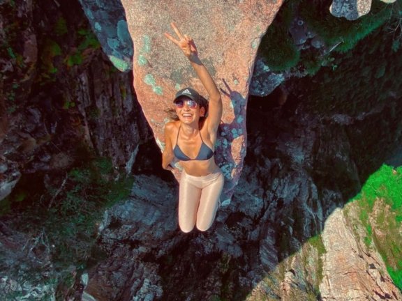 A close-up of a bright green leaf with water droplets, with a lush jungle blurred in the background.